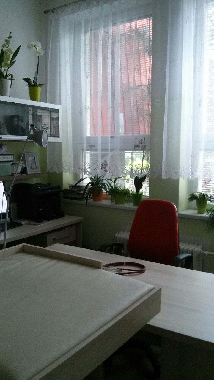 Pediatrická ordinace ve Zbirohu s pracovním stolem, červeným křeslem, tiskárnou a květinami.